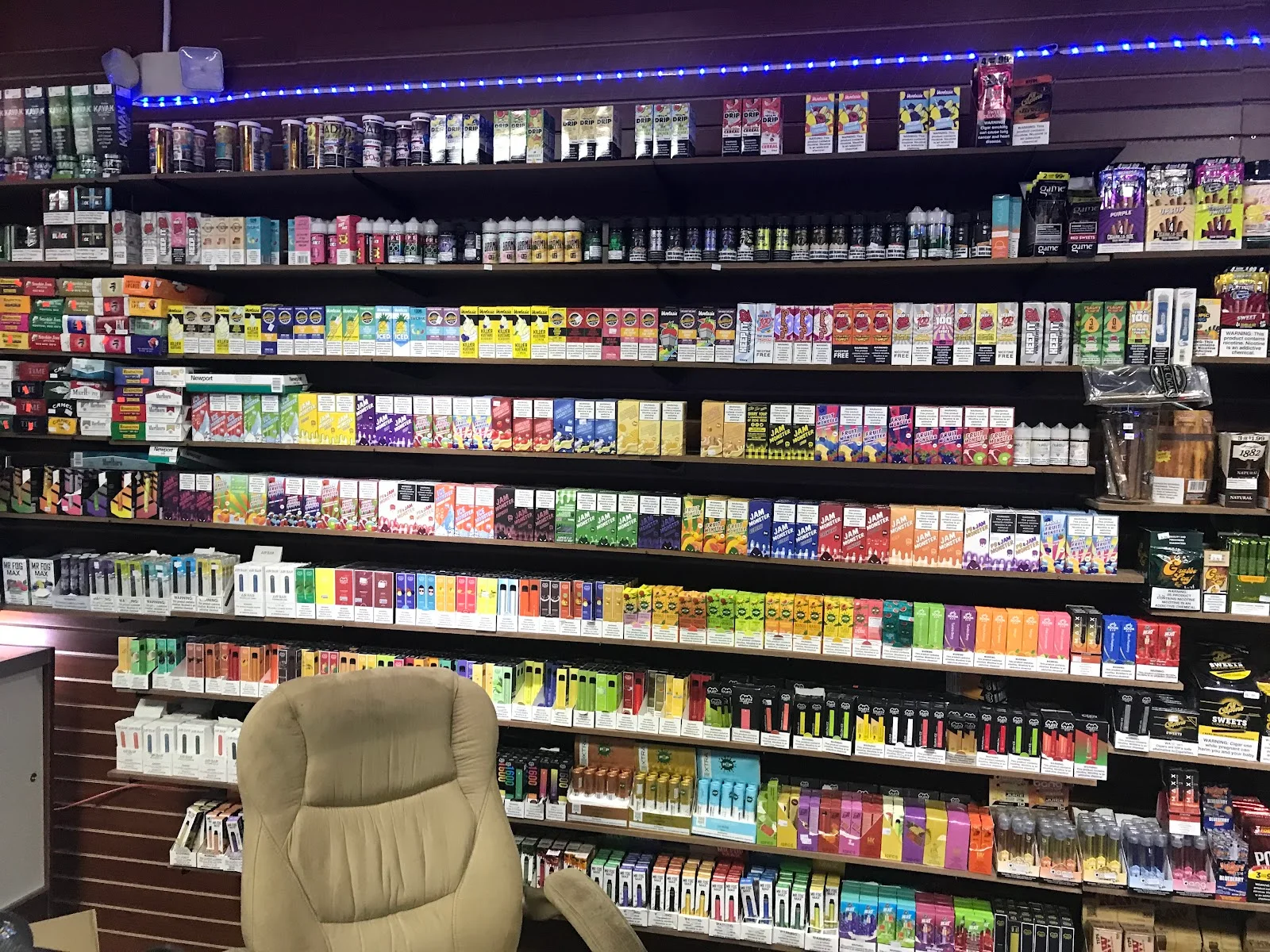 Shop wall stacked with e-liquid bottles, disposable vapes, cigarettes and cigarillos