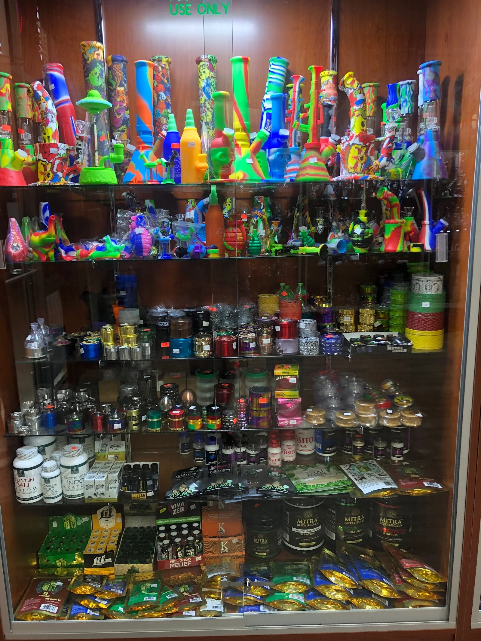 Tall lit cabinet of silicone pipes, grinders, storage jars and kratom packets
